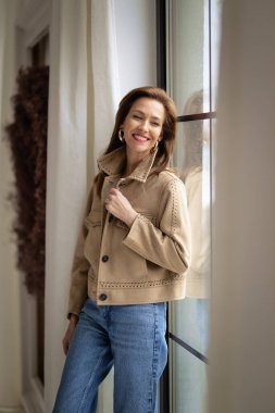 Dairenin penceresinde dinlenirken orta yaşlı bir kadın düşünceli görünüyor. Ceket ve kot giyen güzel bir kadın..  