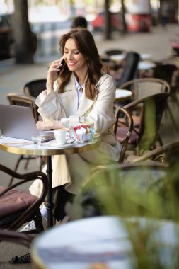Masada oturan çekici bir kadın, açık bir kafede dizüstü bilgisayarla çalışıyor. Trençkot giyen orta yaşlı bir kadın. Kendine güvenen profesyonel kadın iş görüşmesi yapıyor..  
