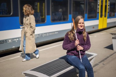 Beyaz bastonlu görme engelli bir kadın tren istasyonunda oturuyor ve birini bekliyor..    
