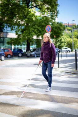Yaya geçidinden geçen beyaz bastonlu kör kadın portresi. Sıradan kıyafetler giyen ve sopasıyla karşıya geçen görme engelli bir kadın. Tam boy çekim. 
