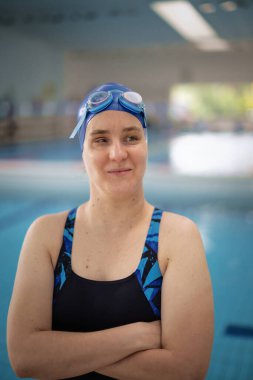 Kapalı bir yüzme havuzunda havuz kenarında duran görme engelli bir kadın. Mayo ve yüzme şapkası takan kendinden emin bir kadın. Yakın çekim..  