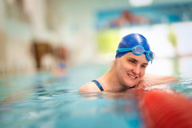 Kapalı havuzda yüzen görme engelli bir kadın. Mayo ve yüzme şapkası takan kendinden emin bir kadın. Yakın çekim..  