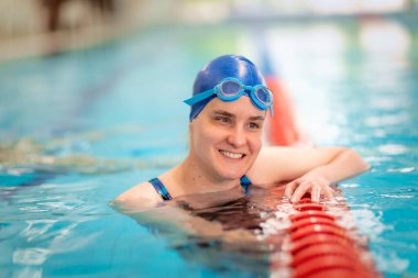 Kapalı havuzda yüzen görme engelli bir kadın. Mayo ve yüzme şapkası takan kendinden emin bir kadın. Yakın çekim..  