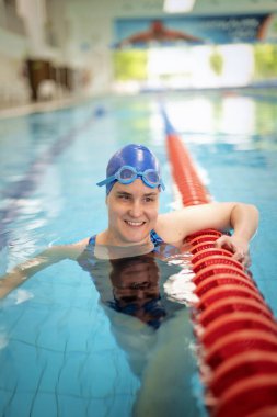 Kapalı havuzda yüzen görme engelli bir kadın. Mayo ve yüzme şapkası takan kendinden emin bir kadın.. 
