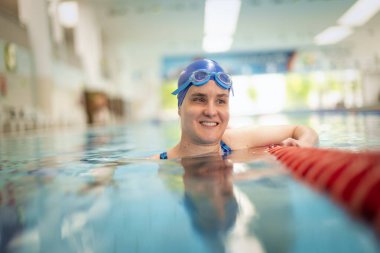 Kapalı havuzda yüzen görme engelli bir kadın. Mayo ve yüzme şapkası takan kendinden emin bir kadın.. 