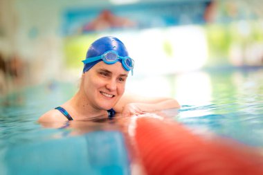 Kapalı havuzda yüzen görme engelli bir kadın. Mayo ve yüzme şapkası takan kendinden emin bir kadın.. 