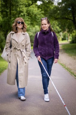 Görme engelli ve işitme engelli bir kadın, kız arkadaşıyla şehirde yürüyor. Görme engelli bir kadın elinde beyaz bir baston tutuyor ve konuşuyor. Tam uzunluk. 