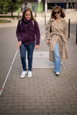 Görme engelli ve işitme engelli bir kadın, kız arkadaşıyla şehirde yürüyor. Görme engelli bir kadın elinde beyaz bir baston tutuyor ve konuşuyor. Tam uzunluk. 