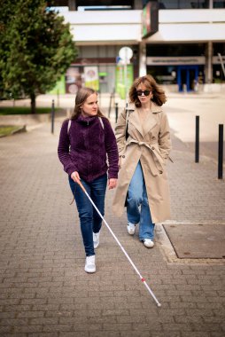Görme engelli ve işitme engelli bir kadın, kız arkadaşıyla şehirde yürüyor. Görme engelli bir kadın elinde beyaz bir baston tutuyor ve konuşuyor. Tam uzunluk. 