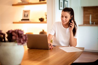 Mutlu kadın akıllı telefon kullanıyor ve evden çalışıyor. Kendine güvenen bir kadın dizüstü bilgisayarının önünde oturuyor ve telefonla konuşuyor. Merkez Ofis. 