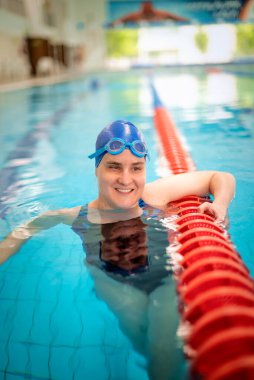 Kapalı havuzda yüzen görme engelli bir kadın. Mayo ve yüzme şapkası takan kendinden emin bir kadın.. 