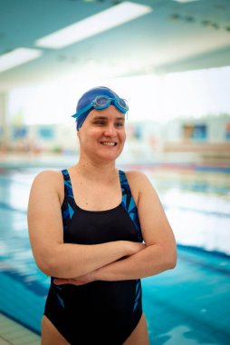 Kapalı bir yüzme havuzunda havuz kenarında duran görme engelli bir kadın. Mayo ve yüzme şapkası takan kendinden emin bir kadın.. 