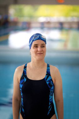 Kapalı bir yüzme havuzunda havuz kenarında duran görme engelli bir kadın. Mayo ve yüzme şapkası takan kendinden emin bir kadın.. 