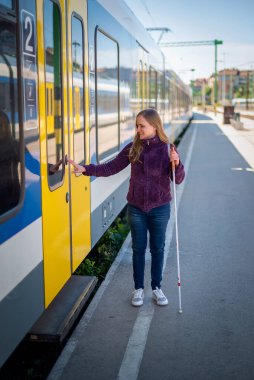 Şehrin dışındaki tren istasyonunda duran beyaz bastonlu kör kadın portresi. Görme engelli bir kadın trene biniyor. Günlük kıyafetler. Tam uzunluk. 