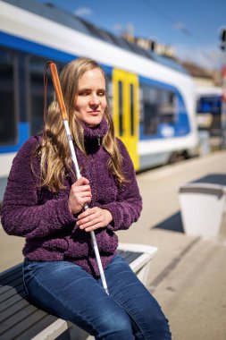 Beyaz bastonlu kör kadın portresi. Şehrin dışındaki tren istasyonunda bankta oturuyor. Treni bekleyen görme engelli bir kadın. Günlük kıyafetler.. 