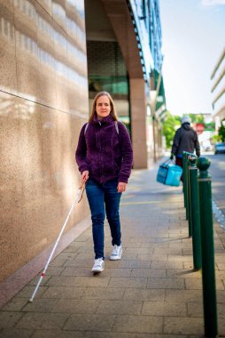 Beyaz bastonlu görme engelli bir kadın şehirde yürüyor. Tam uzunluk. 