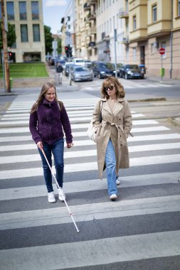 Kız arkadaşıyla yaya geçidinden geçen görme engelli bir kadın var. Tam boy çekim. 