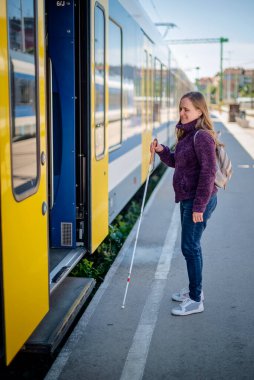 Şehrin dışındaki tren istasyonunda duran beyaz bastonlu kör kadın portresi. Görme engelli bir kadın trene biniyor. Günlük kıyafetler. Tam uzunluk. 