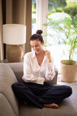 Güzel, mutlu orta yaşlı bir kadının tam boy fotoğrafı rahat koltukta oturuyor, başka tarafa bakıyor, gülümsüyor ve hayal kuruyor.