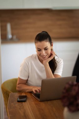 Modern evinde dizüstü bilgisayarlı çekici esmer bir kadın oturuyor. Başarılı bir kadın evde çalışıyor. Merkez Ofis. 