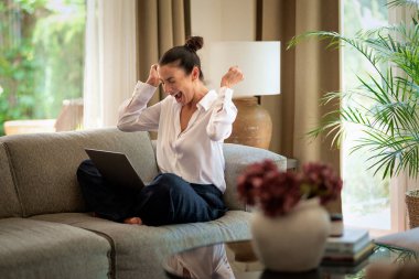 Dizüstü bilgisayar kullanırken koltukta oturan mutlu kadın. Güzel bayan kanepede oturuyor ve başarısının tadını çıkarıyor. Merkez ofis. Tam boy çekim. 