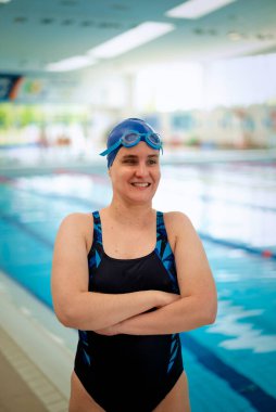 Kapalı bir yüzme havuzunda havuz kenarında duran görme engelli bir kadın. Mayo ve yüzme şapkası takan kendinden emin bir kadın. Yakın çekim.. 