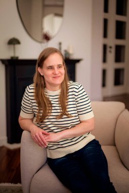 Görme engelli bir kadın evinde, koltukta oturuyor. Sarı saçlı, sıradan kıyafetler giyen bir kadın..