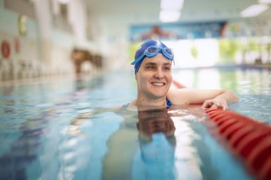 Kapalı havuzda yüzen görme engelli bir kadın. Mayo ve yüzme şapkası takan kendinden emin bir kadın.. 