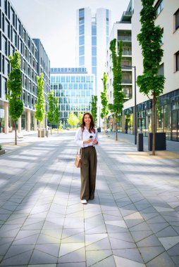 İş yerindeki ofise yürüyen kendine güvenen bir iş kadını. Telefonunu ve mesajlarını kullanan profesyonel bir kadın. Esmer, iş kıyafeti giyen bir kadın. Tam boy çekim. 