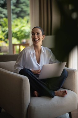 Kumral kadın dizüstü bilgisayar kullanırken koltukta oturuyor. Gündelik kıyafetler giyen güzel bir kadın. Merkez ofis. Tam boy çekim. 
