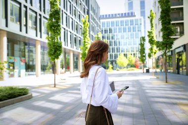 Kendine güvenen bir iş kadını elinde dizüstü bilgisayarla iş bölgesinde dolaşıyor. Orta yaşlı profesyonel akıllı telefon kullanıyor ve iş kıyafeti giyiyor.. 