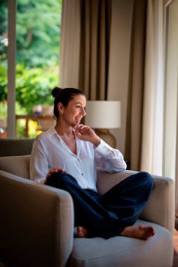 Güzel, orta yaşlı bir kadının rahat koltukta oturup pencereden dışarı bakıp gülümsediği uzun bir sahne.