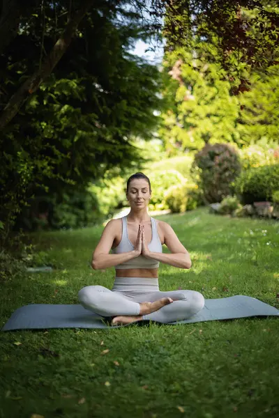 Orta yaşlı kadın arka bahçede tek başına yoga yapıyor. Tam yol ileri. Spor kıyafetleri giyen ve evdeki bahçede meditasyon yapan kendine güvenen bir kadın.. 