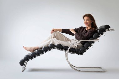 Orta yaşlı, gülümseyen bir kadının modern bir sandalyede dinlenmesi. İzole edilmiş beyaz arka plan. Uzayı kopyala Günlük kıyafetler.. 