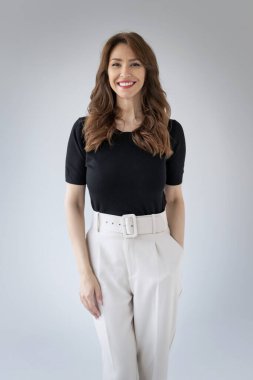 Gülümseyen olgun bir kadının portresi. Beyaz arka planda esmer saçlı, kendinden emin bir kadın. Siyah gömlek ve beyaz pantolon giyen çekici bir kadın. Boşluğu kopyala. 