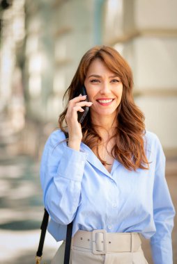 Şehir merkezinde caddeden karşıya geçerken cep telefonuyla konuşan çekici bir kadın. Esmer, günlük kıyafetler giyen, neşeli gülümseyen bir kadın..