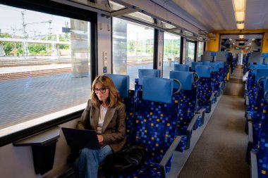 Trenle seyahat ederken dizüstü bilgisayarında çalışan sarışın kadın. Kendine güvenen bir kadın modern bir trende tek başına oturuyor ve dizüstü bilgisayarı üzerinde çalışıyor. Uzaktan kumanda. Tam boy çekim. 