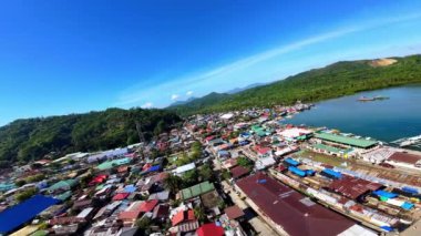 Surigao Del Norte kıyısındaki Placer balıkçı kasabasının etkileyici FPV hava görüntüleri, renkli stilt evler ve mavi gökyüzünün altındaki canlı Filipinli balıkçı topluluğunu gösteriyor..