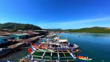 Placer Wharf, Surigao Del Norte, Kuzey Mindanao 'da mavi gökyüzünün altında demirlemiş parlak renkli balıkçı teknelerinin FPV klibi..