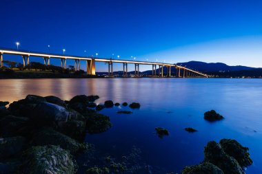 Günbatımında ikonik Tasman Köprüsü açık bir bahar akşamı Hobart, Tazmanya, Avustralya 'daki Derwent Nehri' ni geçer. Clarence 'ın kıyılarından çekildi.