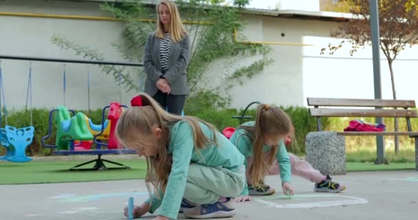 幼儿园的老师看着女孩们用粉笔画画 手里拿着粉笔的女孩在沥青路面上画画 儿童艺术 高质量的4K镜头 — 图库视频影像
