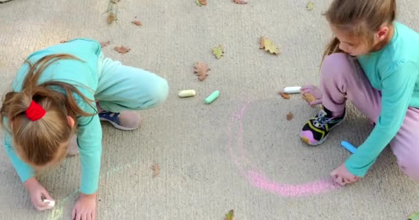 歩道で幸せな子供たちがチョークで描いています 彼女の手でチョークを持った少女はアスファルトを描きます 子供たちのアート 高品質の4K映像 — ストック動画