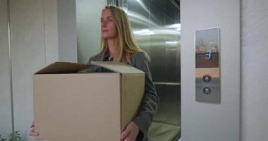 Asansörden çıkan karton kutulu ciddi bir kadın. Kovulmuş ofis çalışanı konsepti. Yüksek kalite 4k görüntü