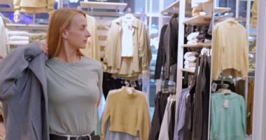 Bayan alışveriş merkezindeki bir giyim mağazasında modern bir palto deniyor. Müşteri dükkandan bir ceket seçer. Yüksek kalite 4k görüntü