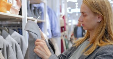 Bayan alışveriş merkezindeki bir giyim mağazasında modern bir palto deniyor. Müşteri dükkandan bir ceket seçer. Yüksek kalite fotoğraf