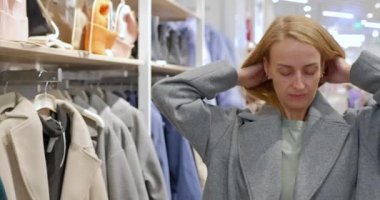 Bayan alışveriş merkezindeki bir giyim mağazasında modern bir palto deniyor. Müşteri dükkandan bir ceket seçer. Yüksek kalite 4k görüntü