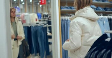 Beyaz giysili genç bir kadın lüks bir butikte beyaz palto deniyor. Yüksek kalite 4k görüntü