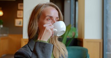 Kafenin camına bakıp beyaz bardaktan kahve içen bir kadın. İşçi kadın öğle yemeğinde kahve içiyor. Yüksek kalite fotoğraf