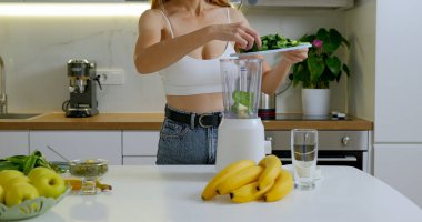Kadın güvertede ıspanak keser ve blender 'a koyar. Sağlıklı meyve püresi konsepti hazırlanıyor. Yüksek kalite fotoğraf