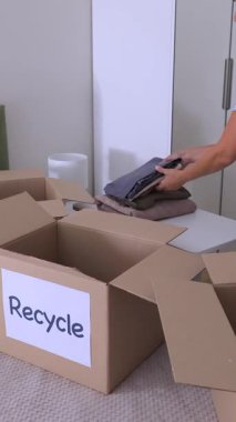 Kadın, sürdürülebilir ev hayatı için kıyafetleri geri dönüşüm kutusuna ayırıyor. Yüksek kalite dikey 4k görüntü